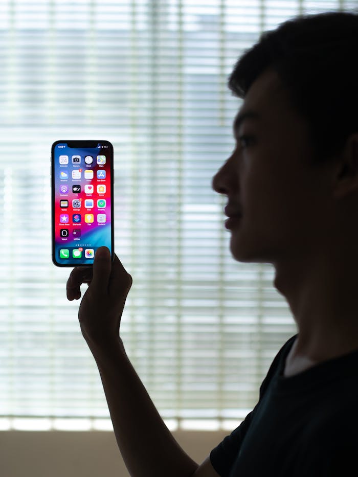pexels-photo-4526398 Profile of a man holding a smartphone with colorful apps, backlit indoors.